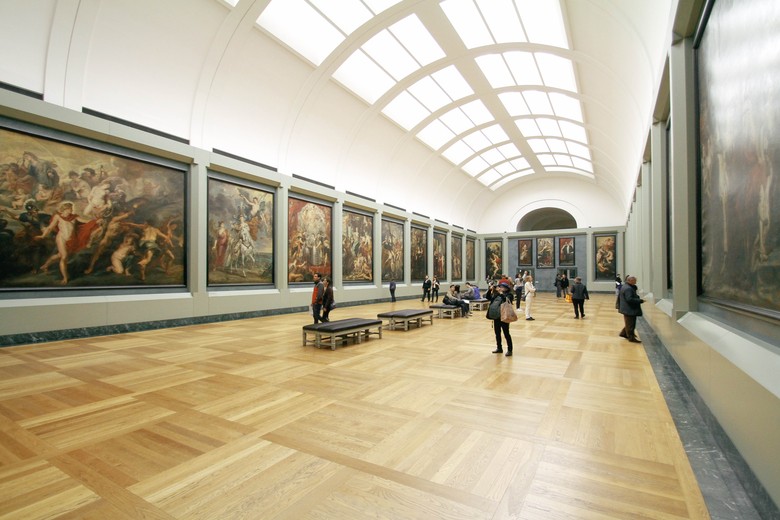 In einem Museumsraum betrachten Personen die dort ausgestellten Gemälde.