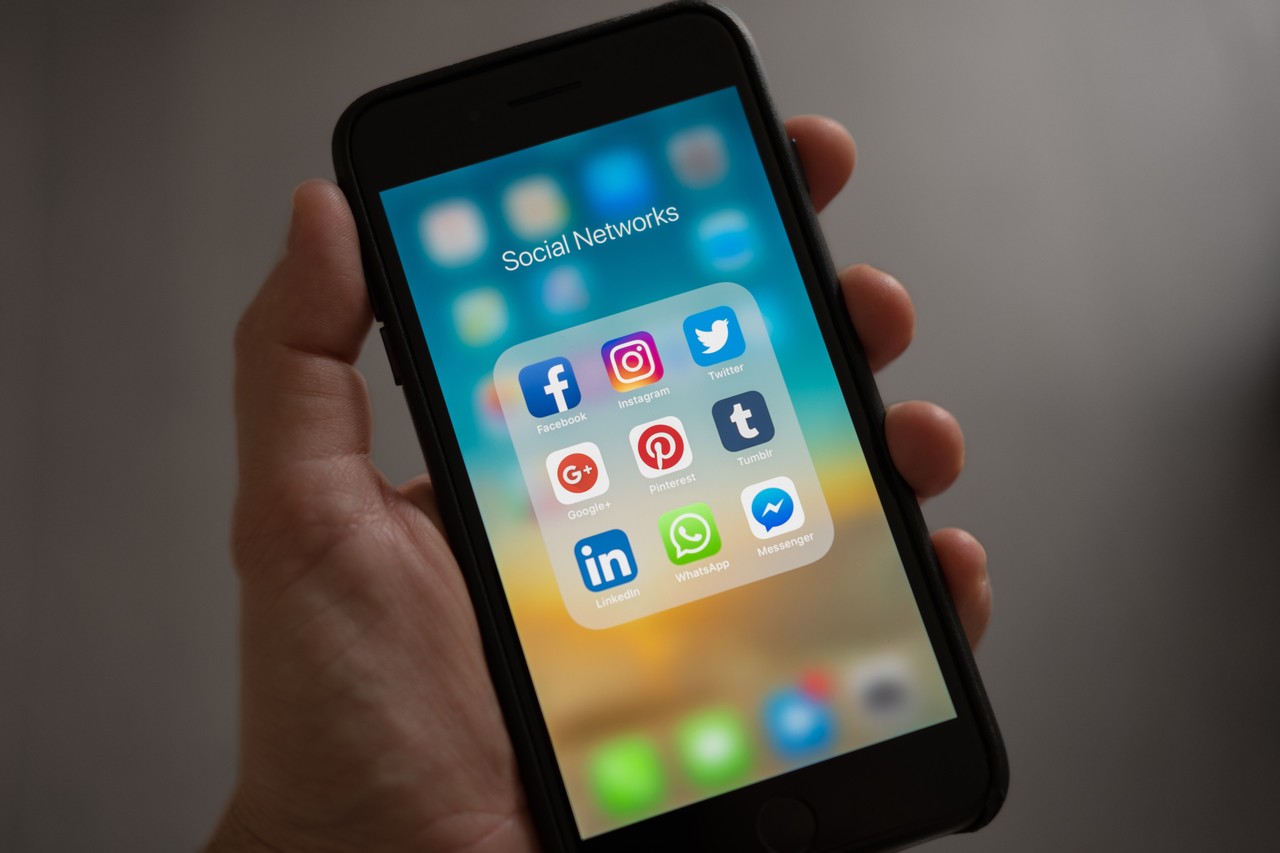 Eine Person hält ein Smartphone in der Hand, auf dessen Bildschirm App-Symbole verschiedener Social Media Netzwerke zu sehen sind.