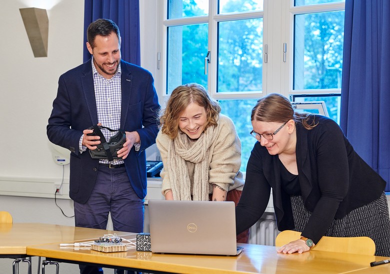 Drei Personen beugen sich lachend über einen Laptop.