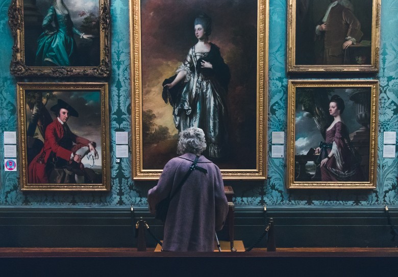 Eine Frau steht vor einer Wand mit Gemälden und betrachtet diese.